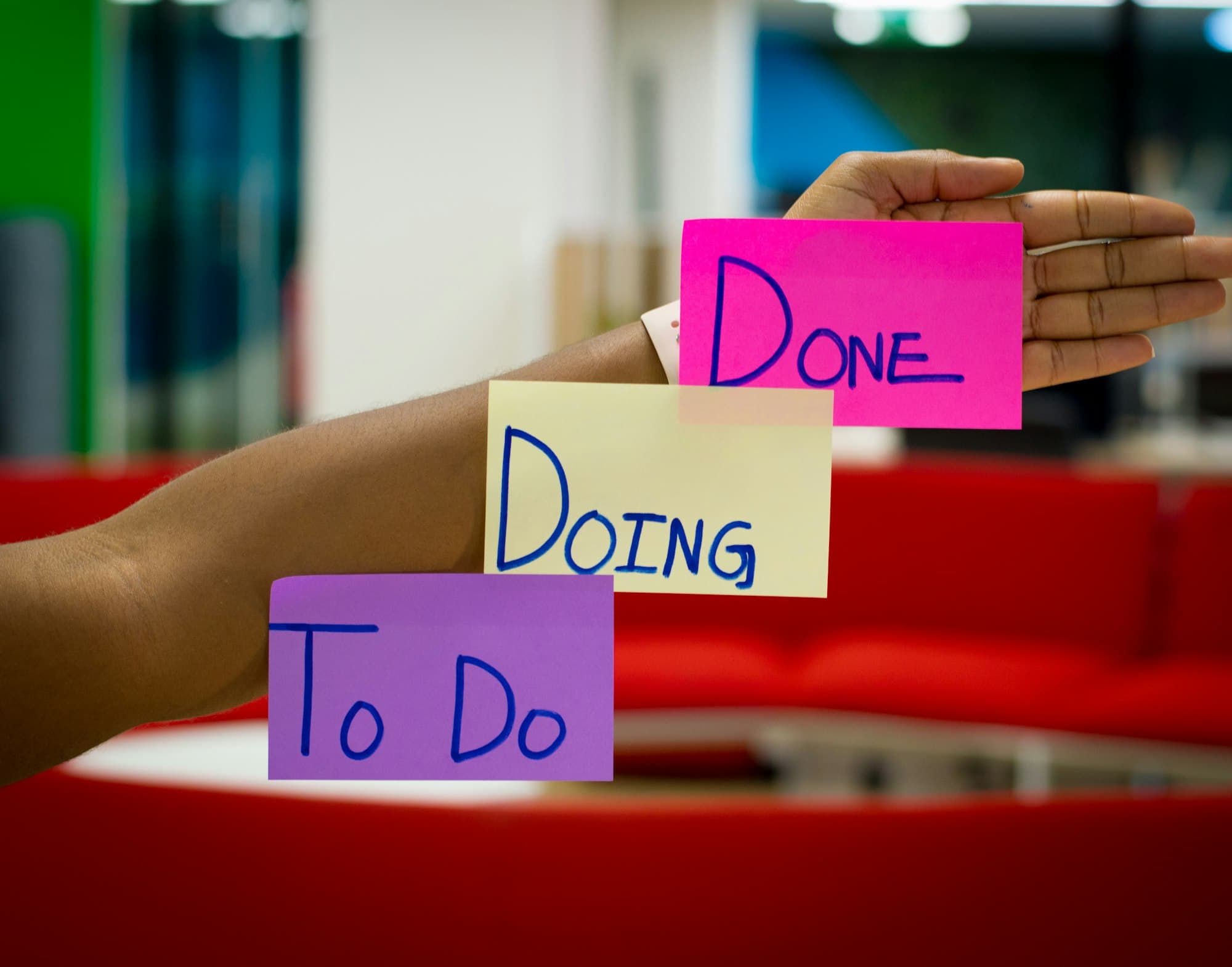 Three sticky notes labelled To Do, Doing and Done held up across an arm
